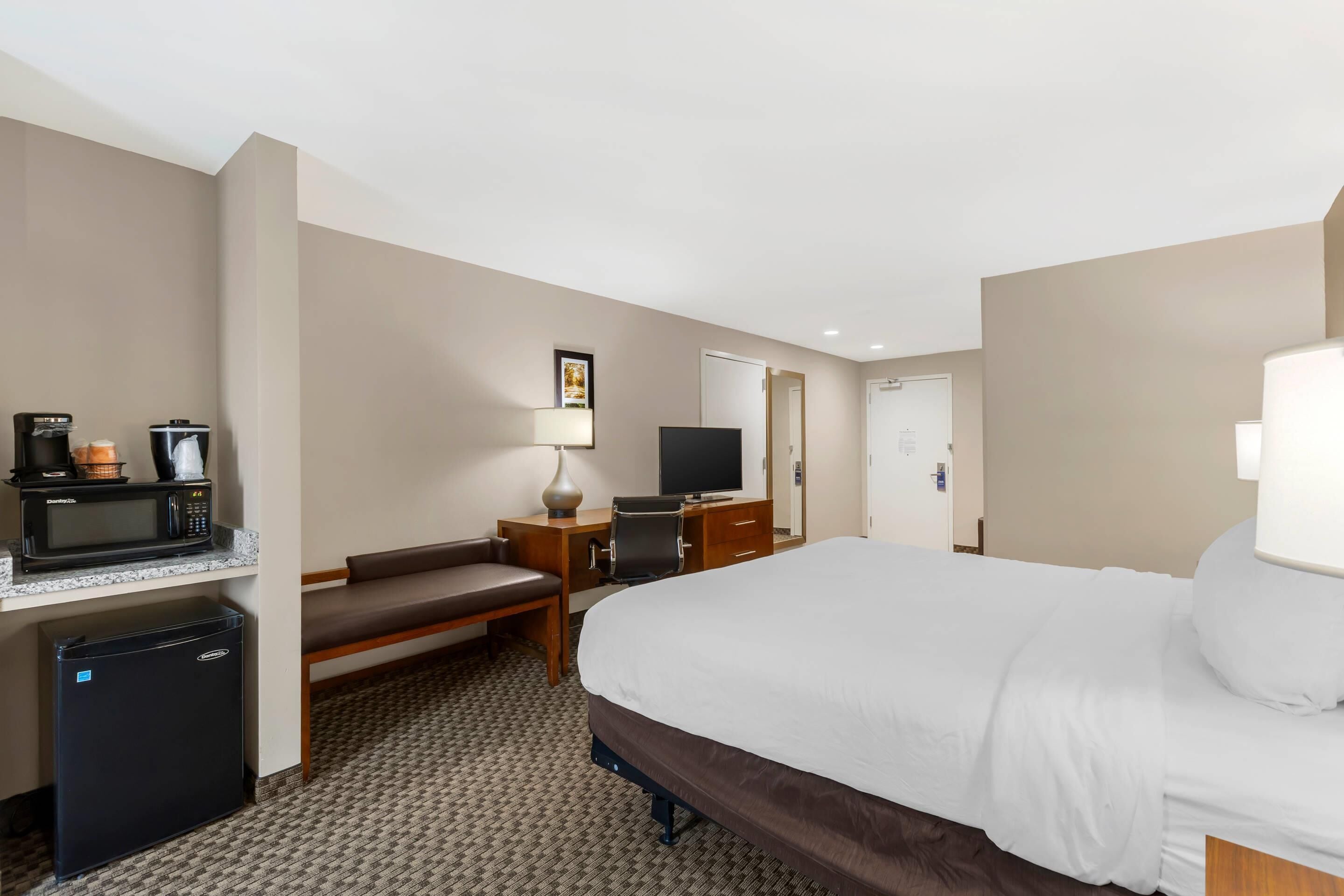 Une chambre d’hôtel équipée d’un lit, d’un bureau avec un micro-ondes, d’un réfrigérateur, d’une télévision et d’une chaise.