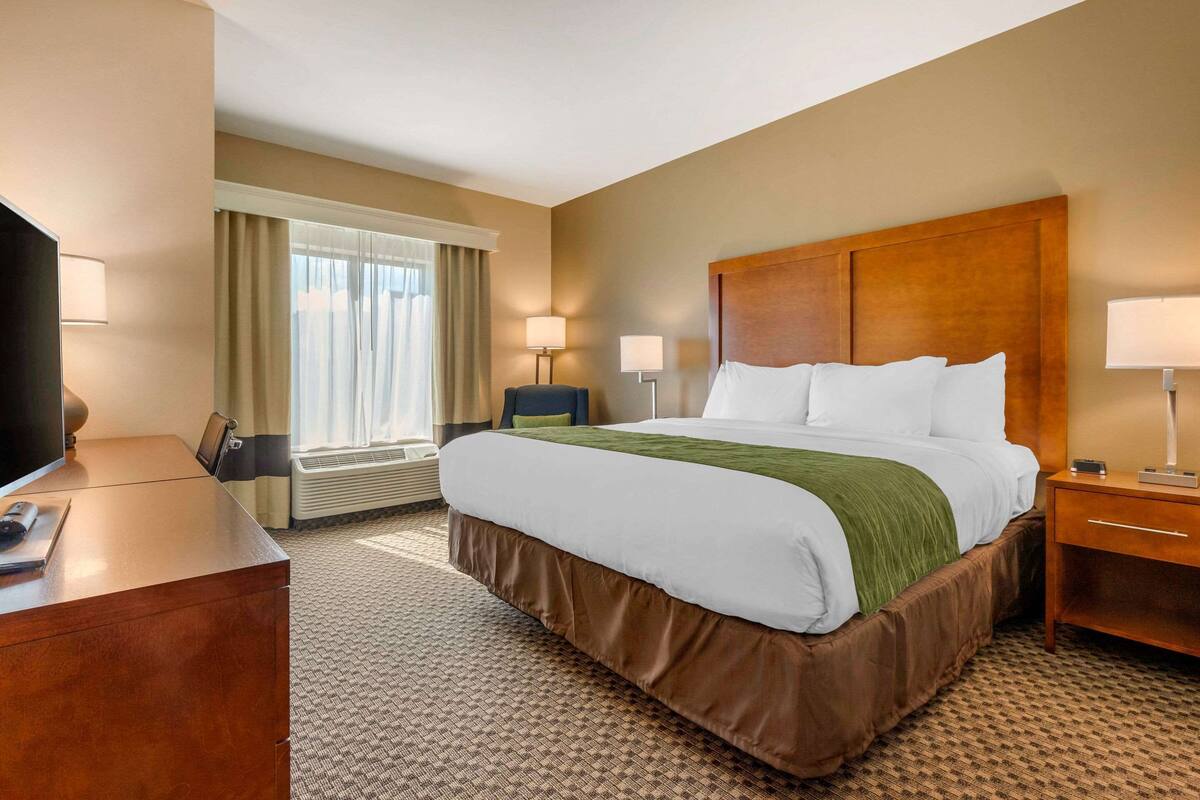A hotel room with a large bed, a desk, a TV, and a window with curtains.