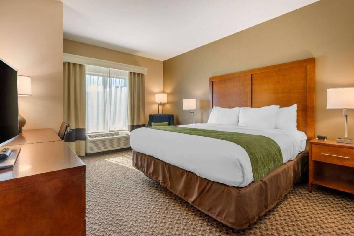 A hotel room with a bed, bedside tables, a desk, a TV, and a window with curtains.