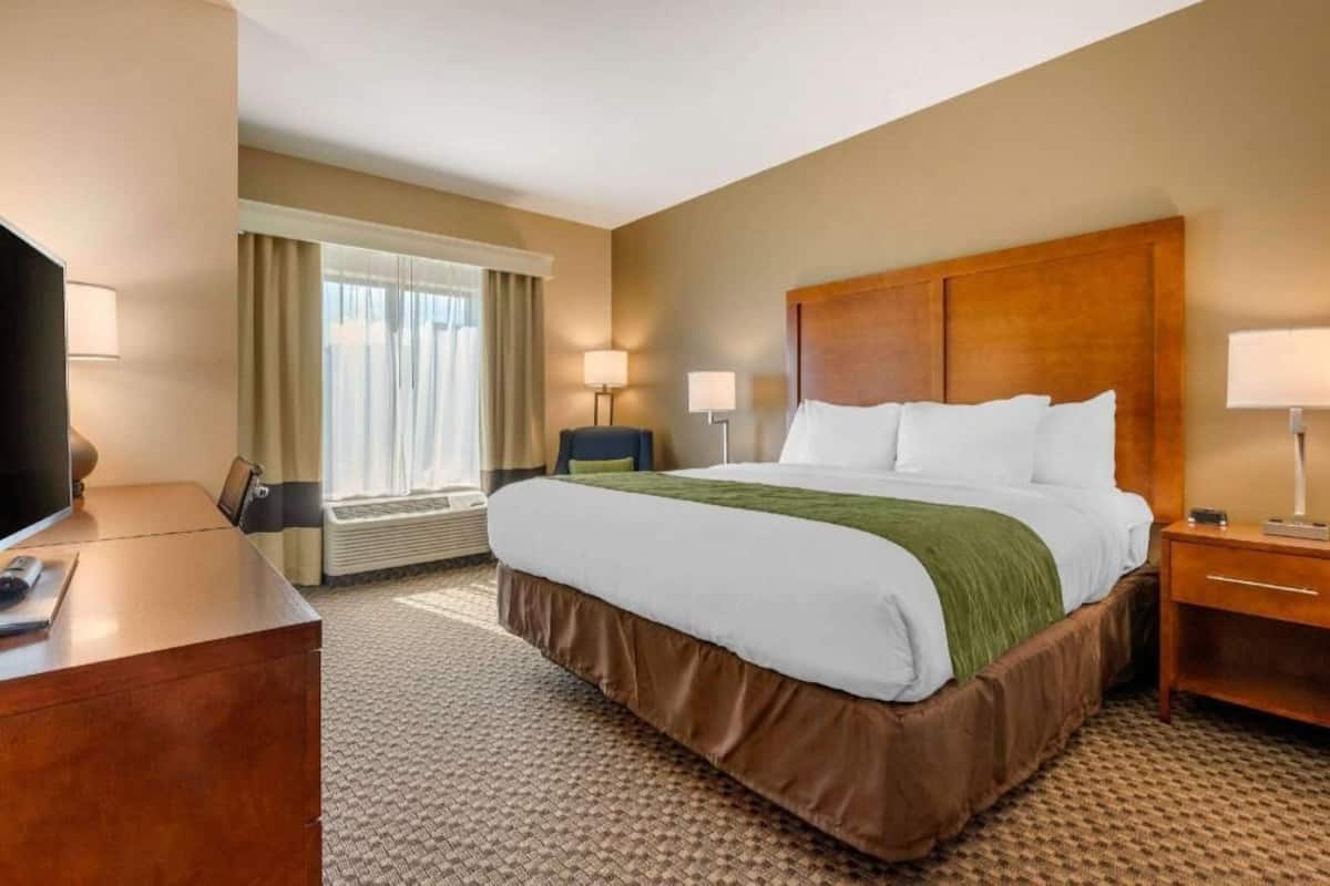 A hotel room with a bed, bedside tables, a desk, a TV, and a window with curtains.