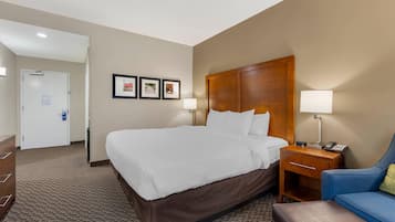 A hotel room with a large bed, a wooden headboard, two bedside tables with lamps, a blue armchair, and a brown sofa.