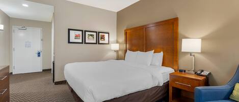 A hotel room with a large bed, a wooden headboard, two bedside tables with lamps, a blue armchair, and a brown sofa.