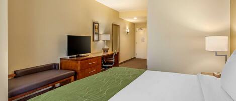 Una habitación de hotel con una cama, un escritorio con televisor, una silla y una lámpara.