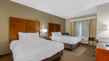 Habitación de hotel con dos camas, un escritorio, una silla y un ventanal con cortinas.