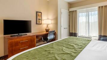 A hotel room with a bed, a desk with a chair, a television, a lamp, and a door.