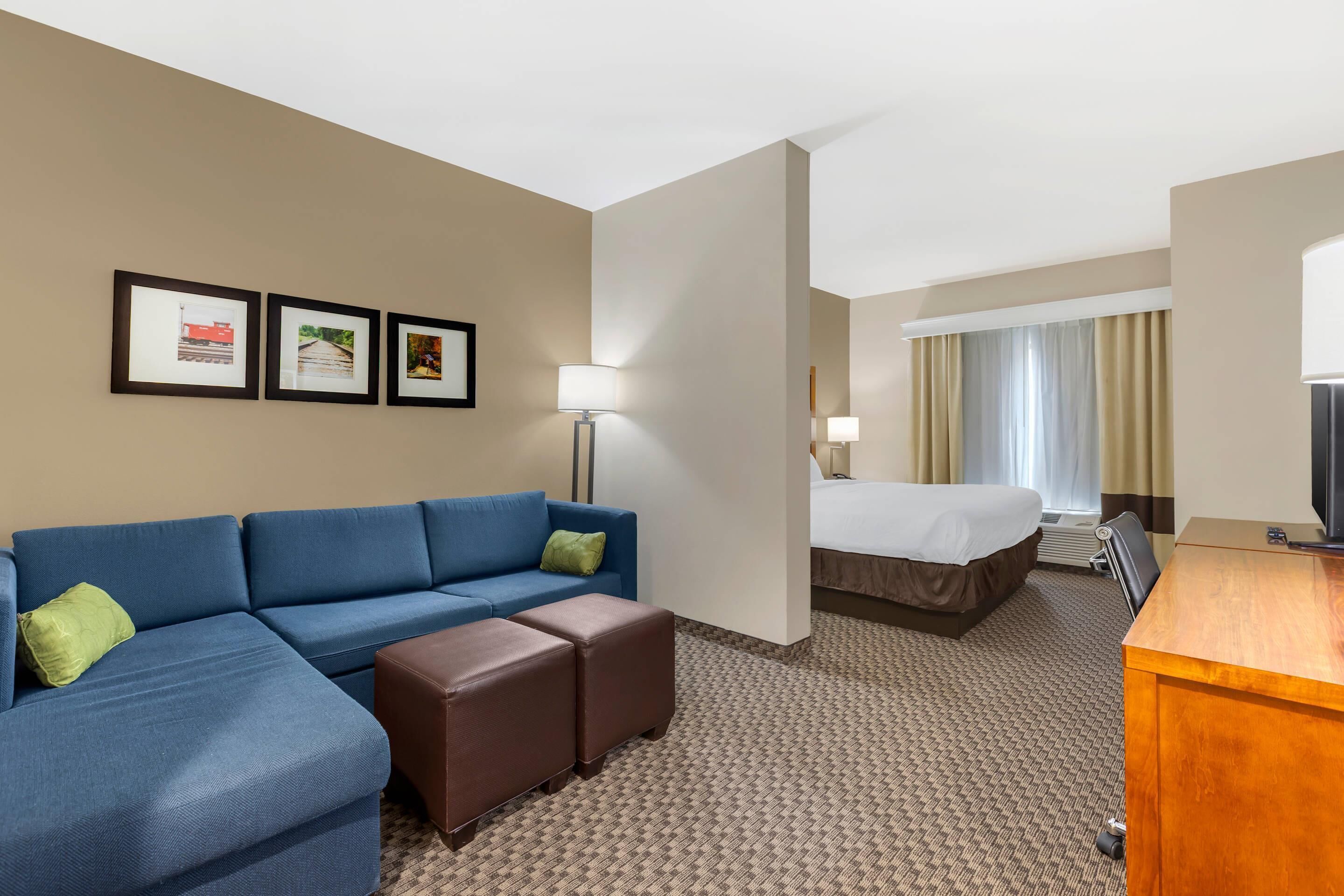 A hotel room with a blue sofa, a bed, a desk, and framed pictures on the wall.