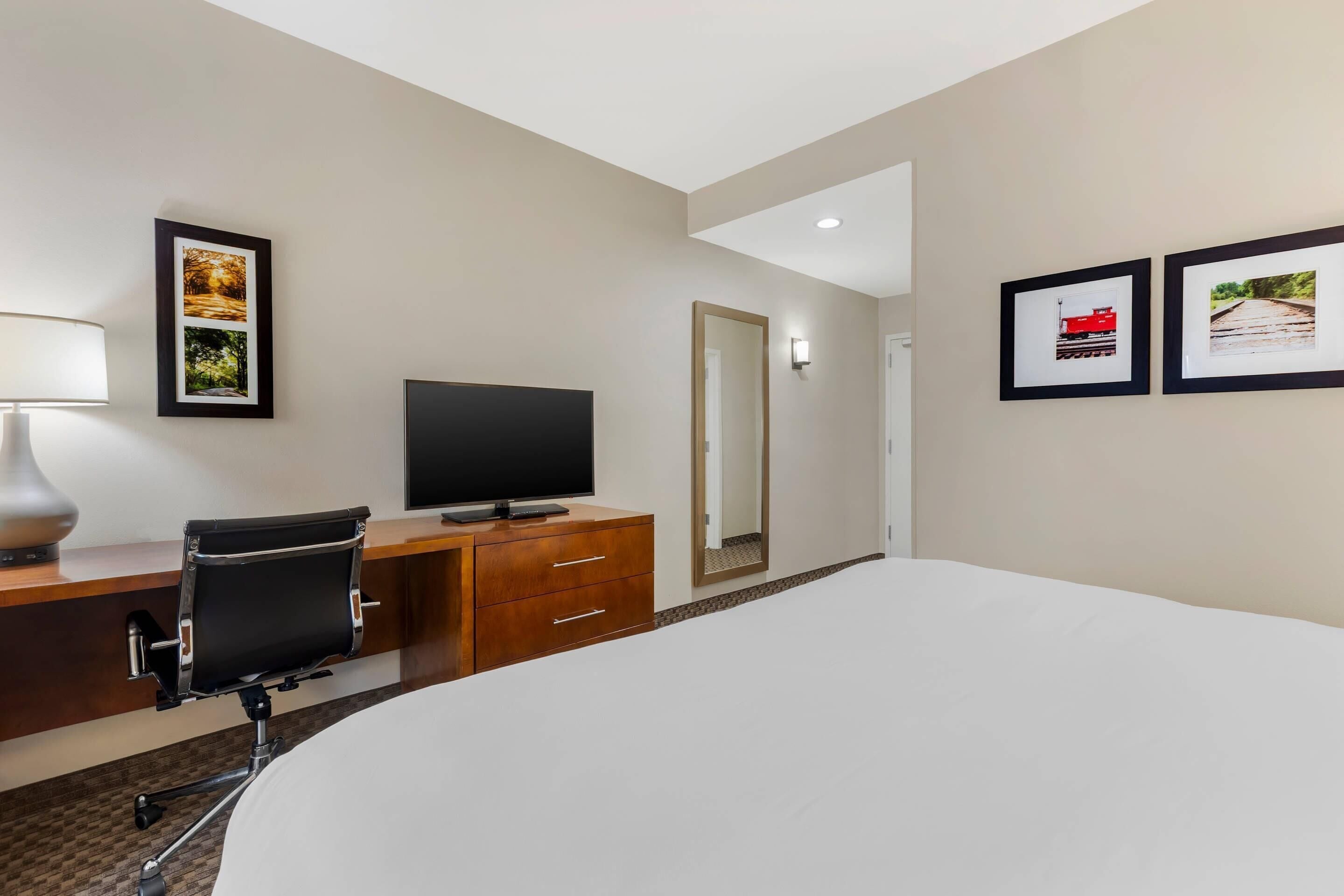 A hotel room with a bed, desk, chair, television, and artwork on the walls.