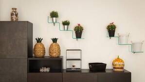 Un salon moderne avec un meuble en bois foncé, une étagère en verre ornée de plantes, un panier en osier et une citrouille décorative.
