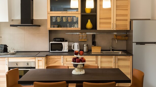 Une cuisine moderne avec des meubles en bois, une hotte noire, un four à micro-ondes et un présentoir à fruits sur la table.