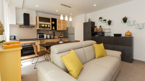 Une cuisine moderne avec des meubles en bois, un coin repas comprenant une table et des chaises, et un salon avec un canapé et des coussins.