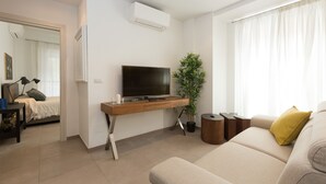 Un salon moderne avec un téléviseur à écran plat posé sur un meuble en bois, un canapé, une plante en pot et une fenêtre avec des rideaux.
