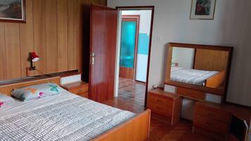 Una camera da letto con un letto, un comodino, una cassettiera, uno specchio e una porta che conduce a un'altra stanza.
