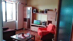 A living room with a television, speakers, and a red chair. There is a window with curtains, a radiator, and a plant on the table. - Very Spacious Apartment (Izola)