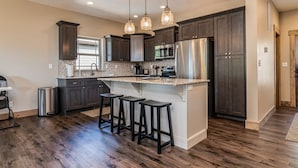 A kitchen with dark wood cabinets, a stainless steel refrigerator, a microwave, and a large island with bar stools.