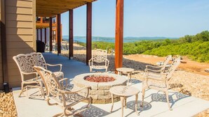 An outdoor patio with wicker chairs and a fire pit, overlooking a scenic landscape.