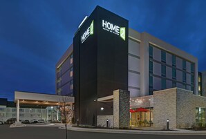 A modern hotel with a prominent "HOME 2" sign, a covered entrance, and a visible outdoor seating area.