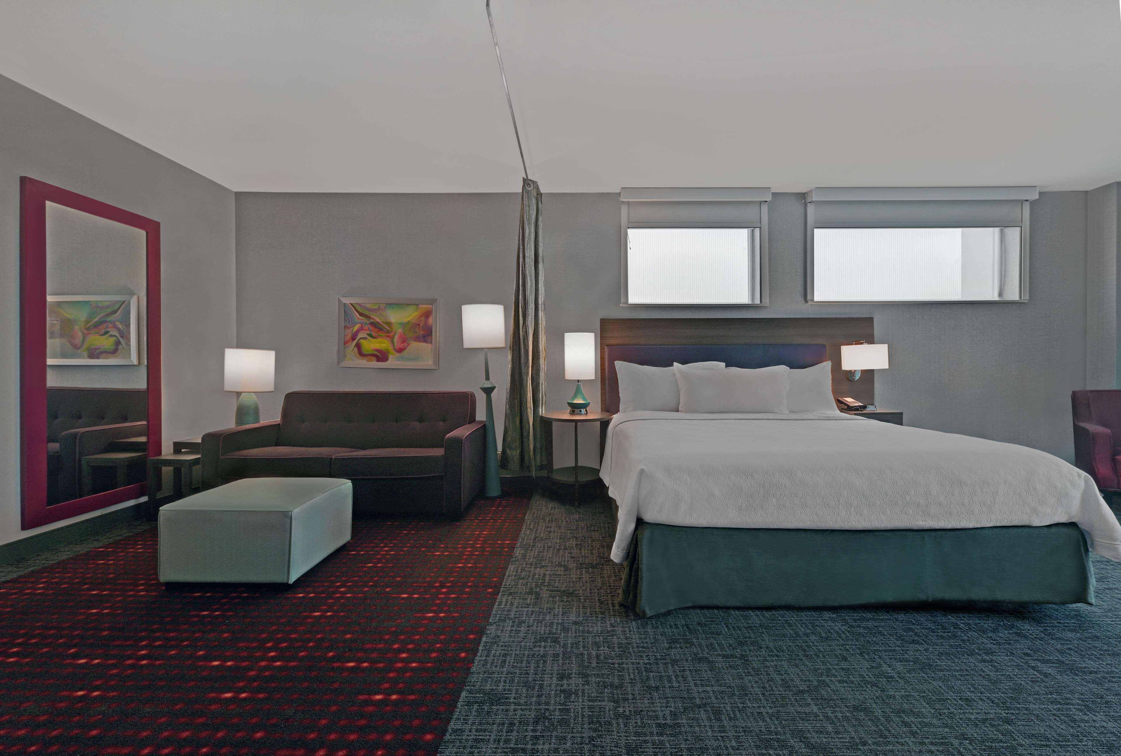 A hotel room with a bed, a sofa, a chair, a small table, and two bedside lamps.