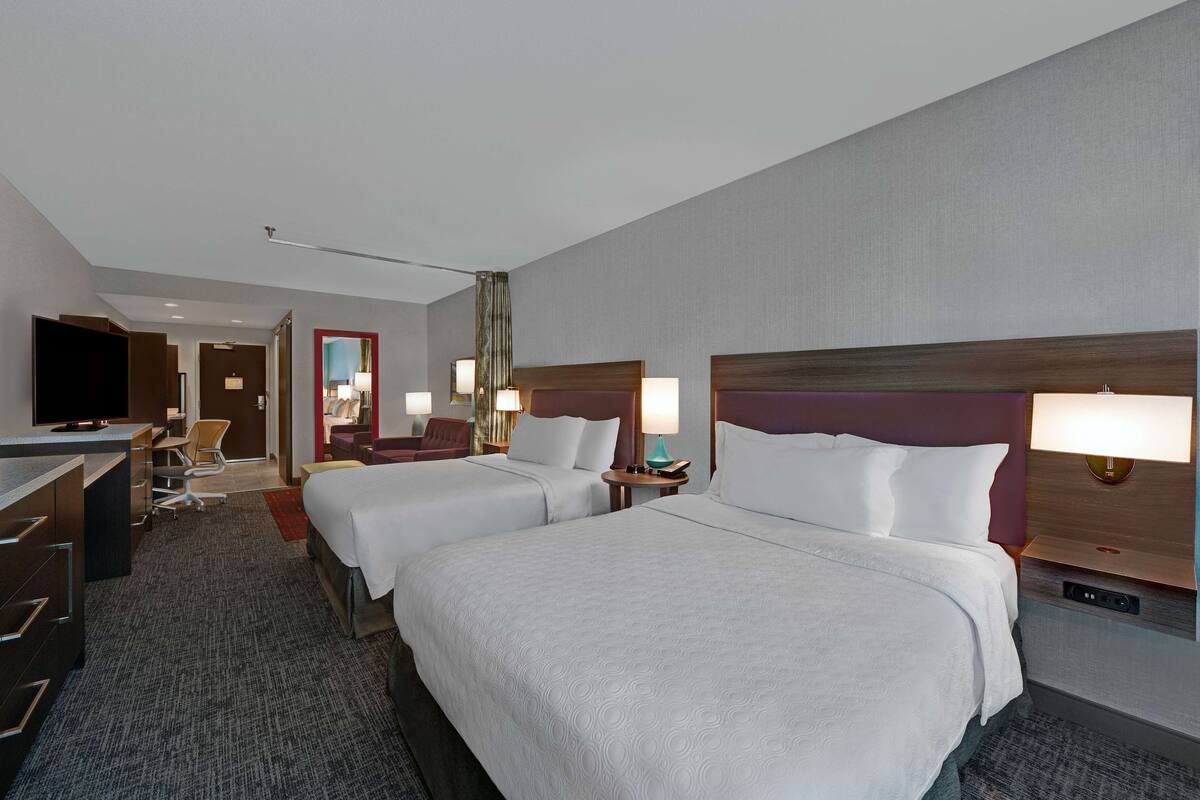 Ein Hotelzimmer mit zwei Betten, einem Schreibtisch, einem Fernseher und einem durchgehenden Türspalt sichtbaren Badezimmer.