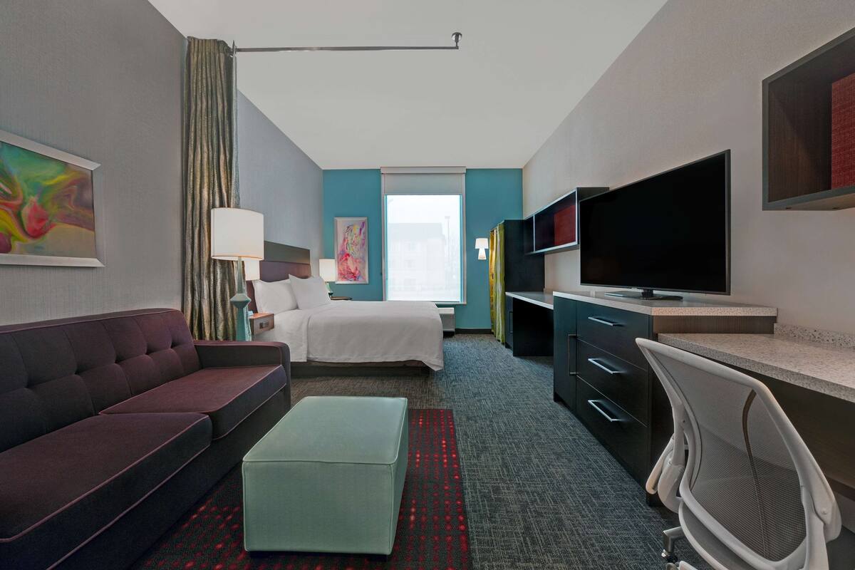 Ein Hotelzimmer mit Bett, Sofa, Schreibtisch, Fernseher und Fenster.