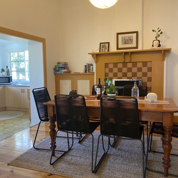A dining area with a wooden table, black chairs, a checkered fireplace, and a kitchen in the background.
