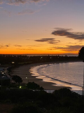 A coastal sunset view with a beach and distant city lights.