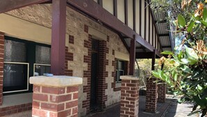 A building with a brick facade, a covered porch with wooden beams, and a stone pathway leading to the entrance.