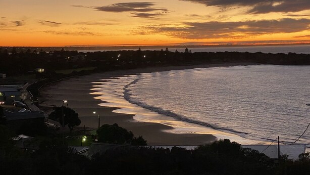 A coastal sunset view with a beach, ocean waves, and distant shoreline.