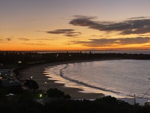 A coastal sunset view with a beach, ocean waves, and distant shoreline.