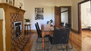 A dining area with a wooden table, chairs, a hanging light fixture, a fireplace, and a wall-mounted picture.