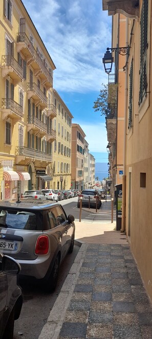 Eine enge Straße gesäumt von mehrstöckigen Gebäuden, parkenden Autos und einem sichtbaren Hotelschild.