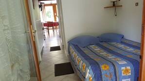 Een slaapkamer met een bed, een deur naar een eethoek en een betegelde vloer.