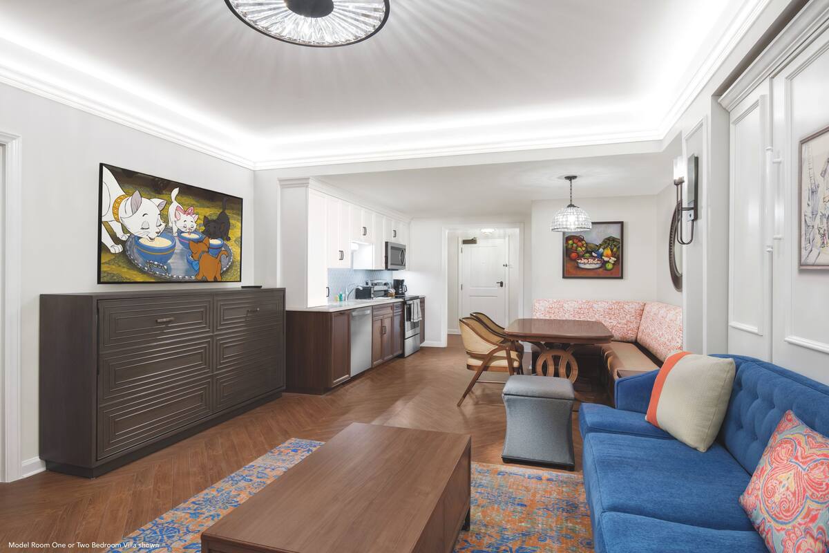 A modern living room with a blue sofa, wooden coffee table, and a dining area with a kitchen in the background.