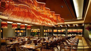 A spacious restaurant with multiple dining areas, a distinctive ceiling design, and large windows offering a view of the sunset.