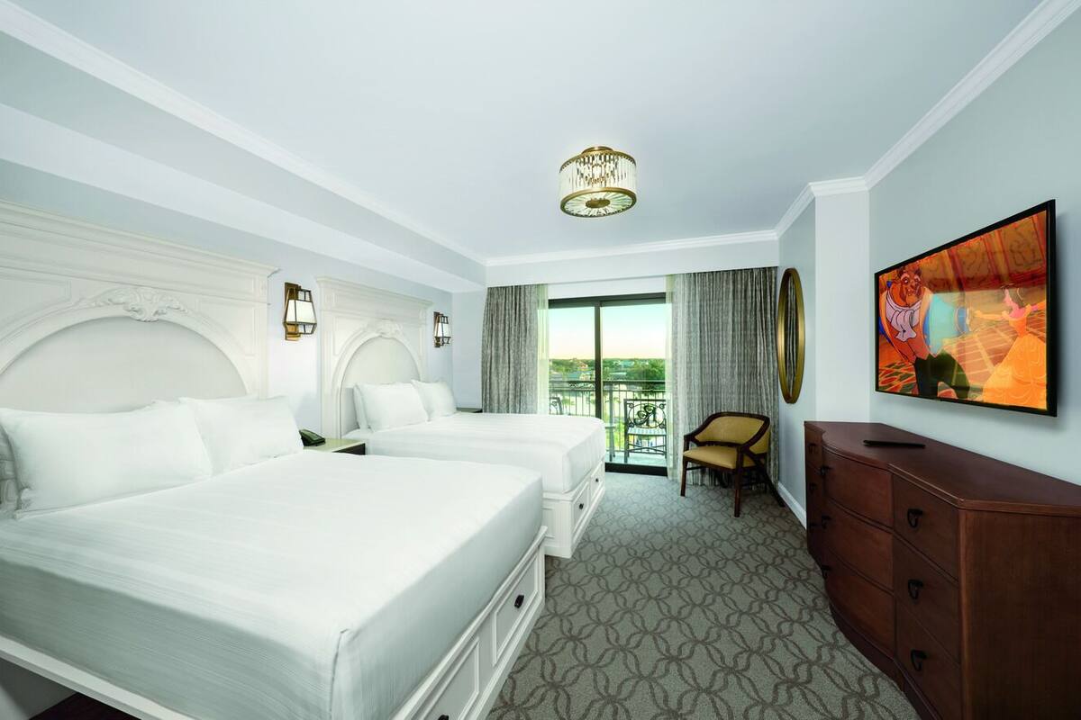 A hotel room with two beds, a chandelier, a TV, and a balcony with a view.