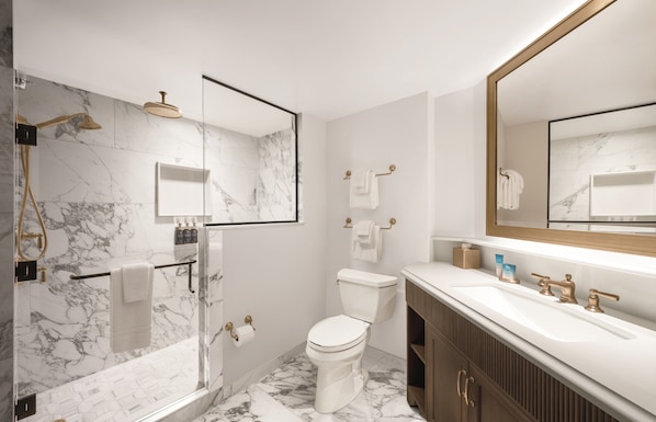 A modern bathroom with a marble shower, a toilet, a sink with a large mirror, and wooden cabinets.