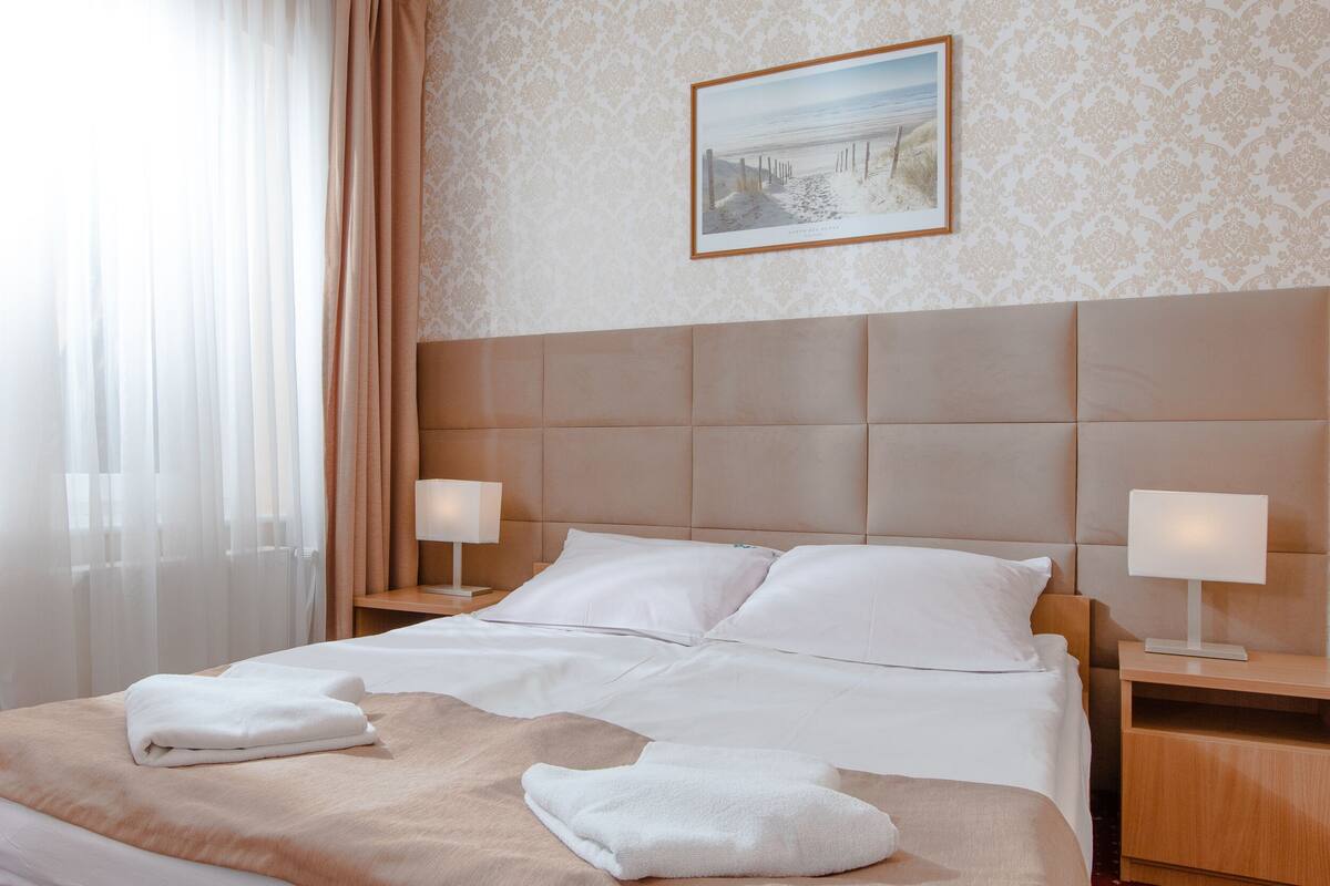 A neatly made bed with white linens, two bedside lamps, and a framed picture on the wall.