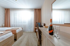 Quarto de hotel com duas camas, uma escrivaninha com computador, uma garrafa de vinho e dois copos.