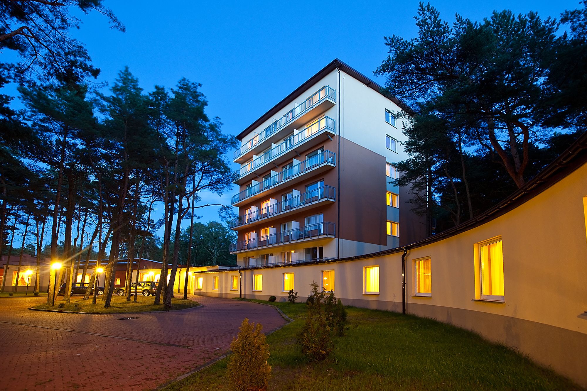 Un hotel de varios pisos con balcones, un camino de entrada pavimentado y un exterior bien iluminado.