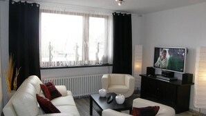 A modern living room with a sofa, armchair, and a television on a stand. - At the gates of Hamburg in the old country (Mittelnkirchen)