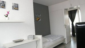 A small, modern bedroom with a single bed, a desk with a chair, and a door leading to another room. - At the gates of Hamburg in the old country (Mittelnkirchen)