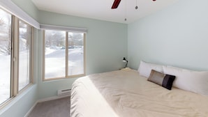 A bedroom with a large window, a bed with white bedding, and a ceiling fan.