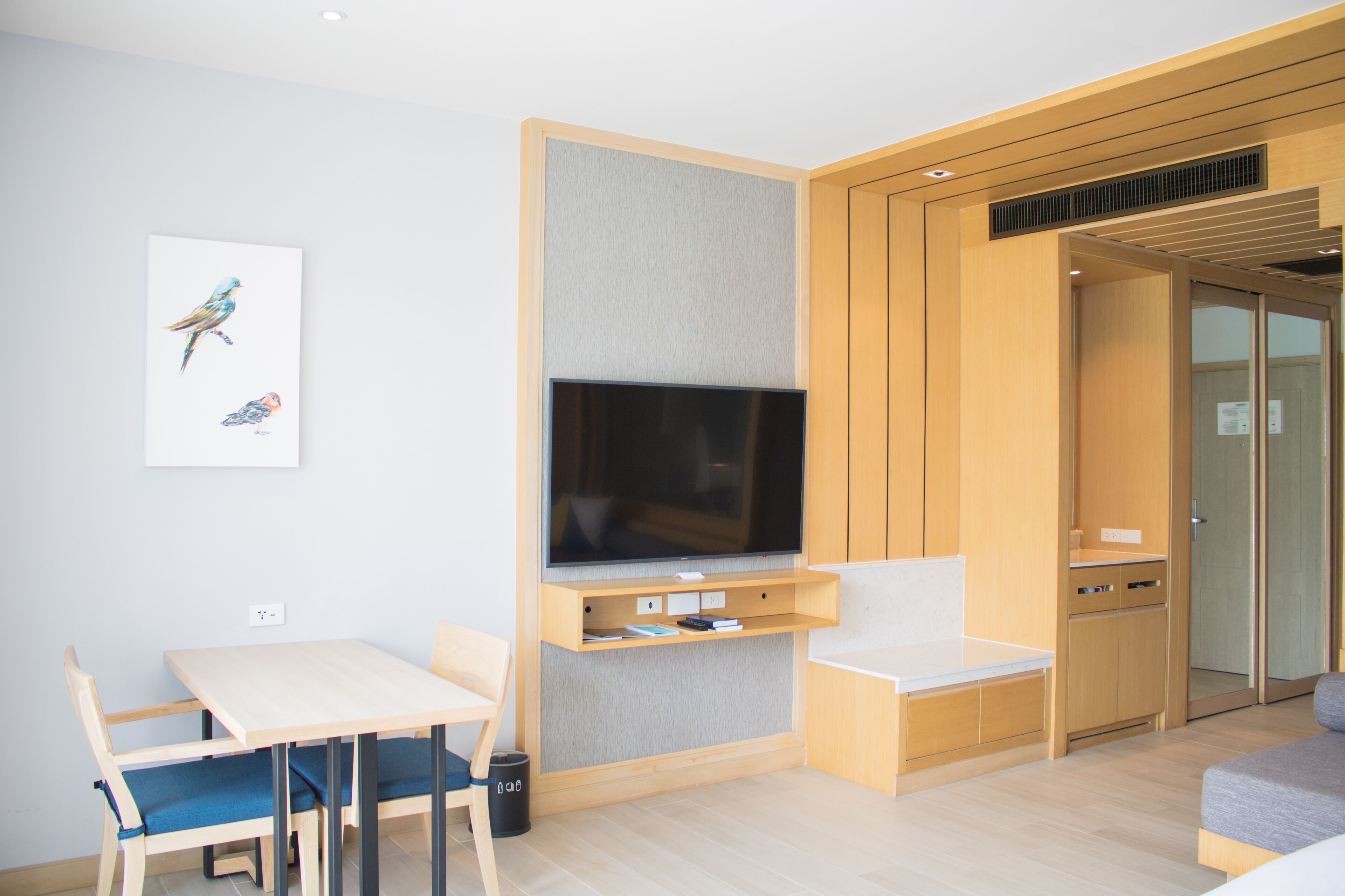 A modern room with a flat-screen TV mounted on a wooden panel, a small table with chairs, and a sofa.