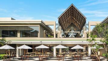 A modern building with a unique geometric roof structure, outdoor seating area with tables and umbrellas, and a mix of indoor and outdoor spaces.