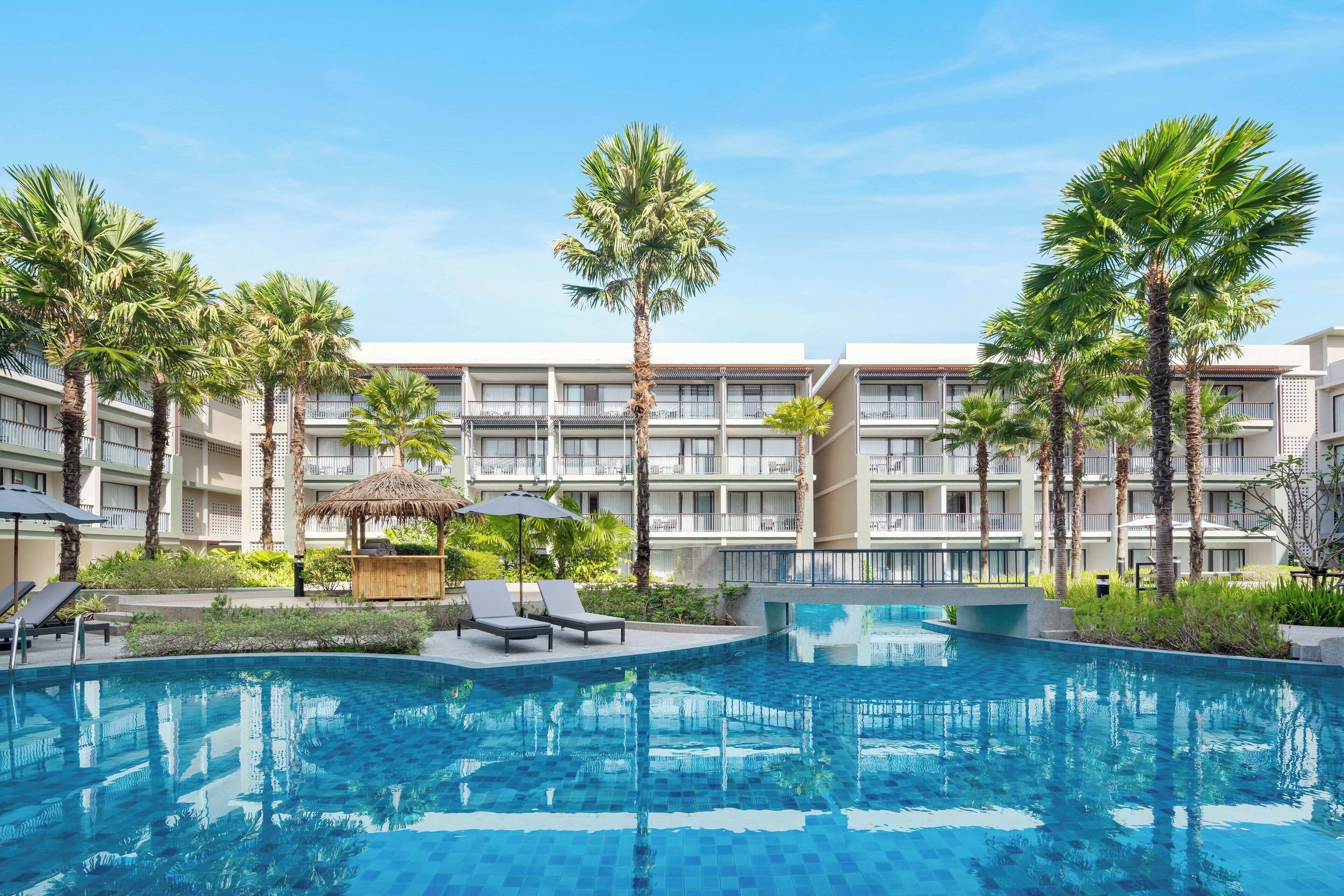A hotel with a swimming pool surrounded by palm trees and lounge chairs.