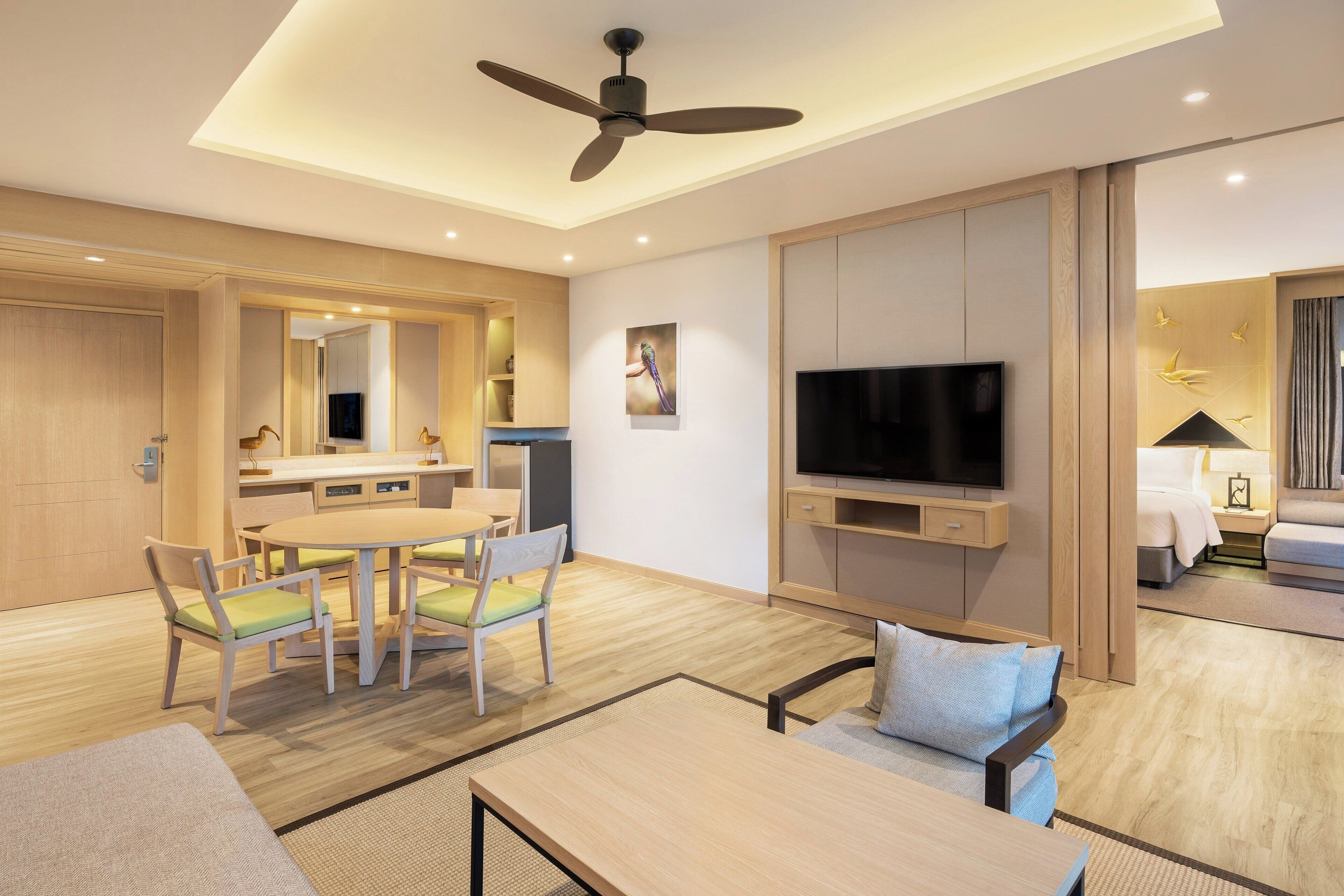 A modern hotel room with a dining area, a TV, a ceiling fan, and a bed.