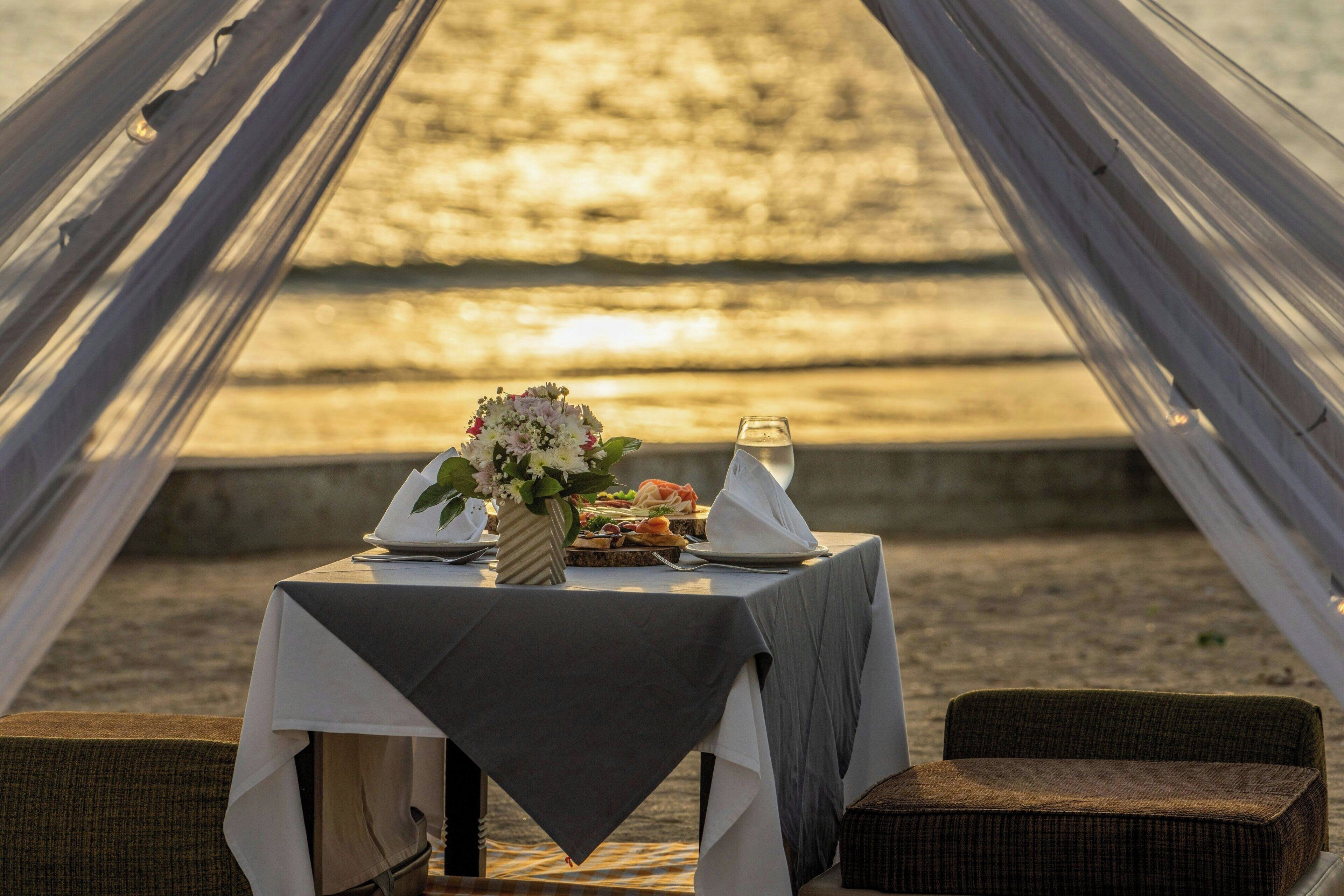 Une table dressée pour deux personnes, avec vue sur la mer, agrémentée d’un arrangement floral et d’un verre d’eau.