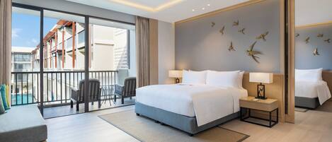 A modern hotel room with a large bed, two bedside tables, a seating area with a chair and a small table, and a balcony with a view of the city and a pool.