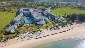 Vue aérienne d’un complexe hôtelier comprenant plusieurs bâtiments, une grande piscine et une plage avec des transats.