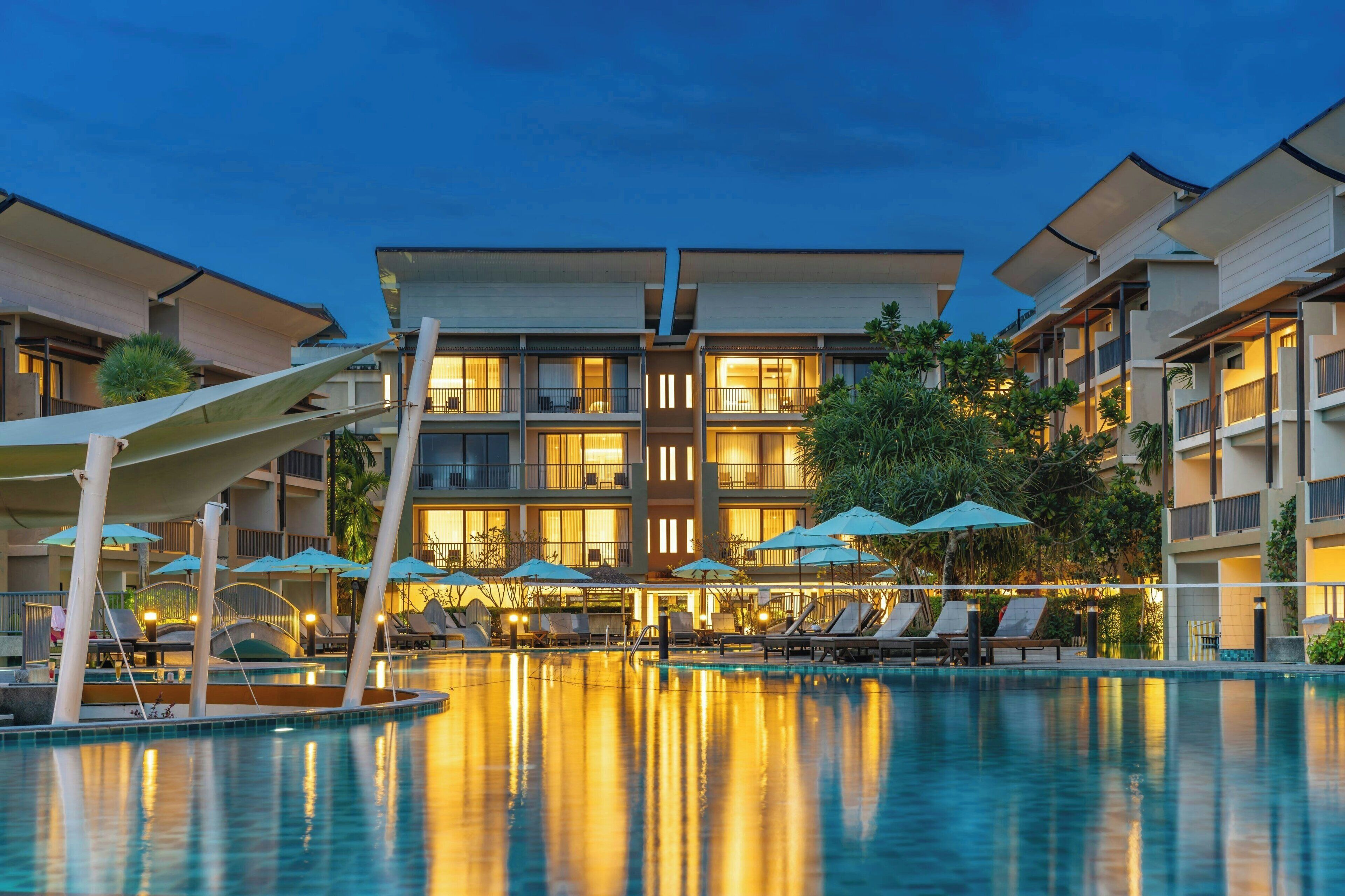 A hotel with a pool area, multiple balconies, and outdoor umbrellas.