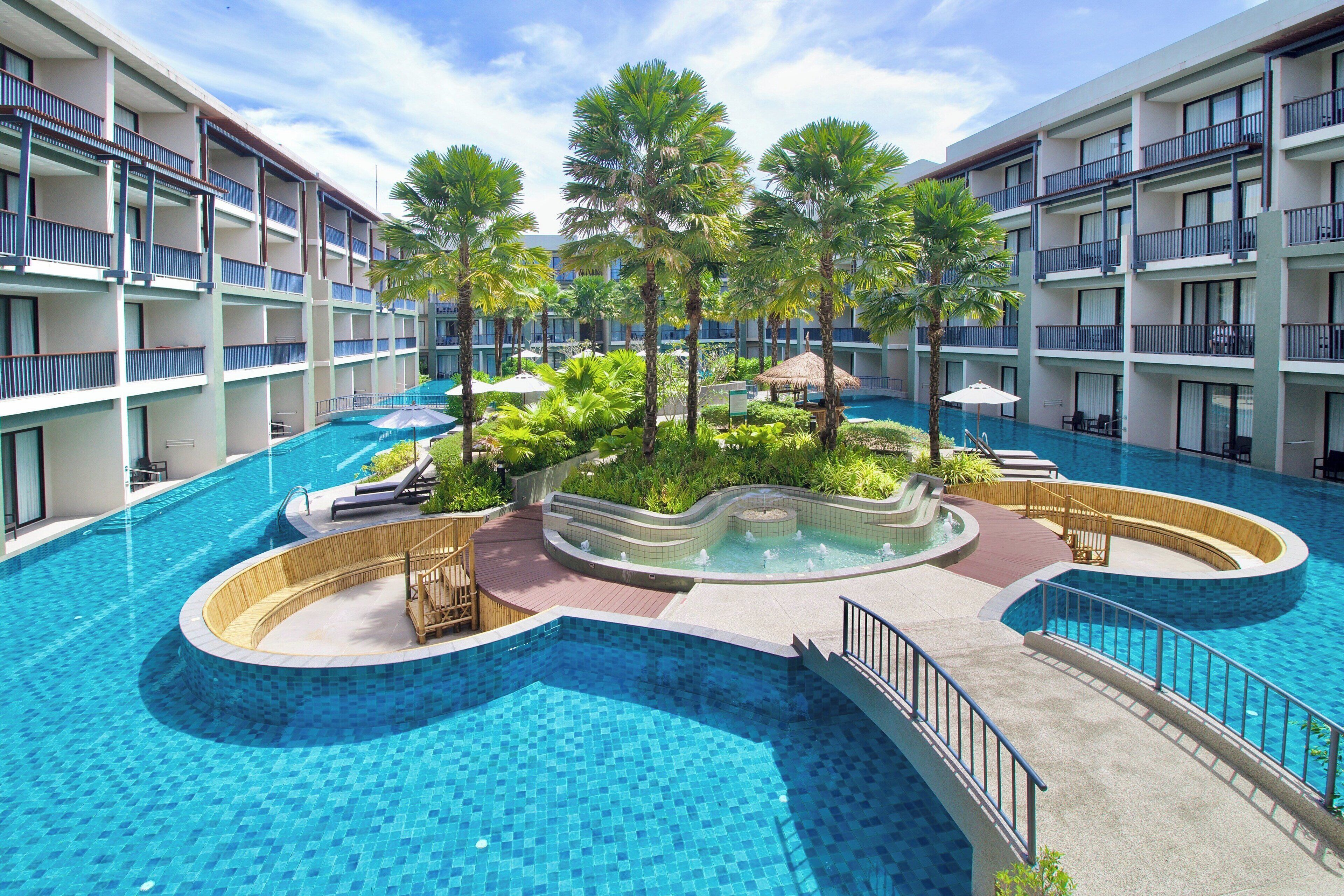 A multi-level hotel with a central swimming pool surrounded by palm trees and lounge areas.